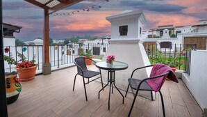 A covered patio with a table and chairs, potted plants, and a view of buildings in the background. - Casa de la Abuelita w/Private Pool & Volcano View (San Pedro Las Huertas)