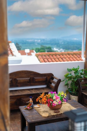 A wooden table with a doll, a bowl of flowers, and a view of a cityscape through a window. - Casa de la Abuelita w/Private Pool & Volcano View (San Pedro Las Huertas)