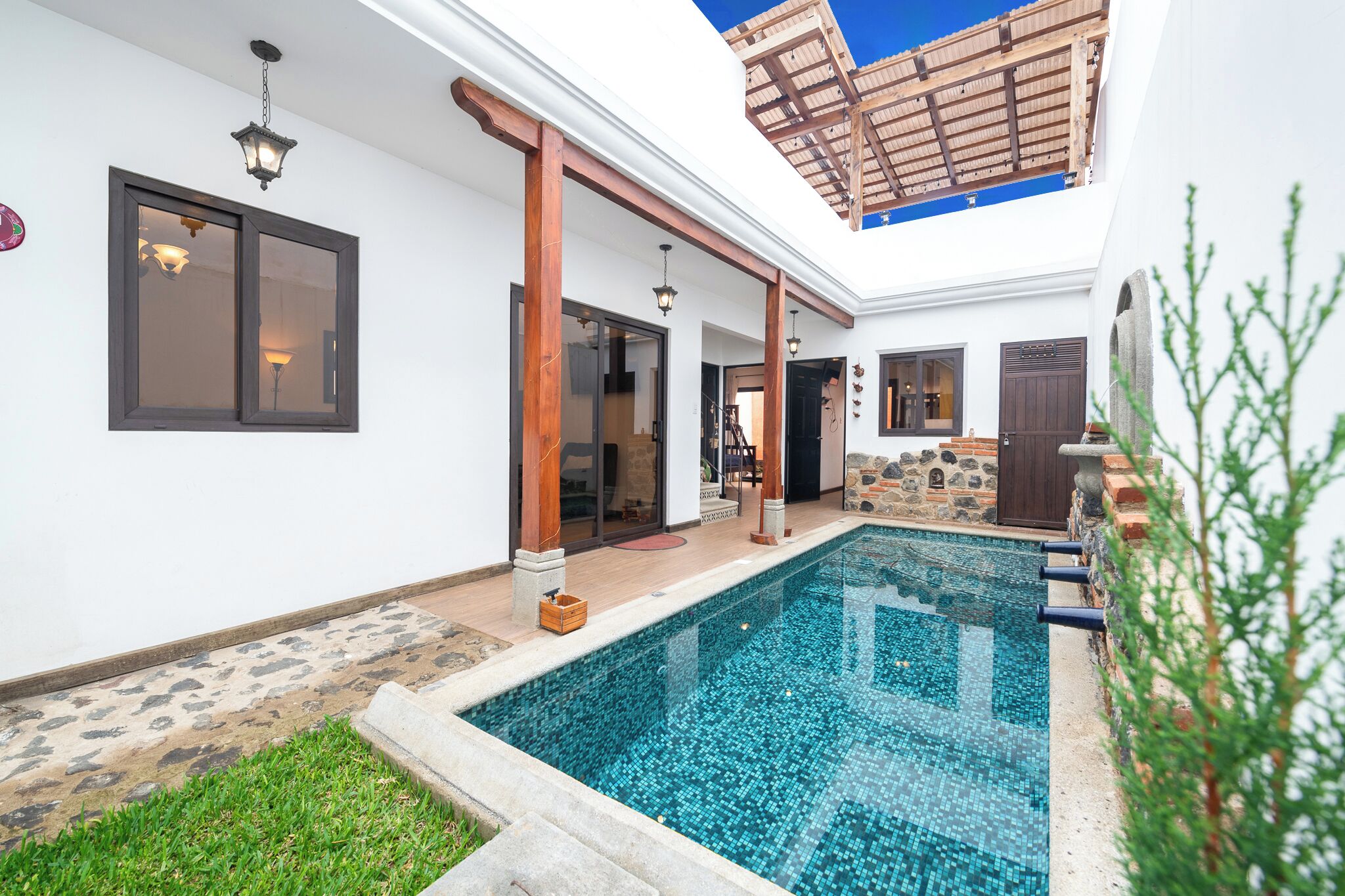 A swimming pool with a tiled deck, a pergola, and a stone wall.