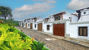 A row of white buildings with wooden doors and balconies, a cobblestone street, and green landscaping. - Casa de la Abuelita w/Private Pool & Volcano View (San Pedro Las Huertas)