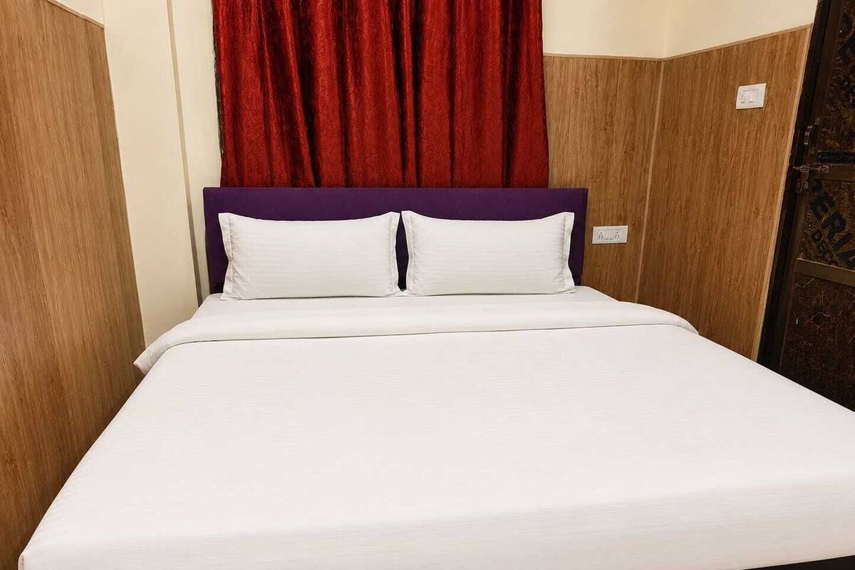 A single bed with white bedding and a purple headboard, set against a wooden wall with a red curtain.