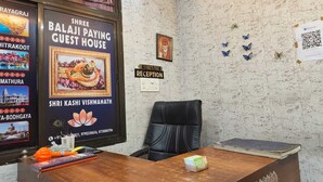A reception desk with a framed poster, a black leather chair, and a stack of books. - Shree Balaji Paying Guest House (Varanasi)