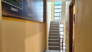 A hallway with a staircase, a trash bin, and a poster on the wall. - Shree Balaji Paying Guest House (Varanasi)