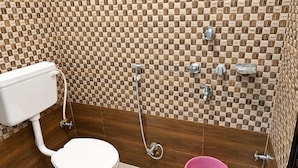 A bathroom with a toilet, a shower, and a pink bucket. - Shree Balaji Paying Guest House (Varanasi)