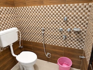 A bathroom with a toilet, a shower, and a pink bucket. - Shree Balaji Paying Guest House (Varanasi)