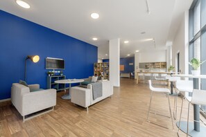 A modern interior with a blue accent wall, a sofa, a small table, a bar area, and a kitchen in the background. - Rosedale Court (Newcastle-upon-Tyne)