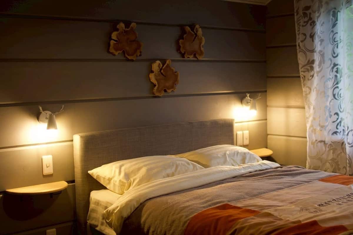 Una cama con sábanas blancas, dos lámparas de noche y decoración en la pared.