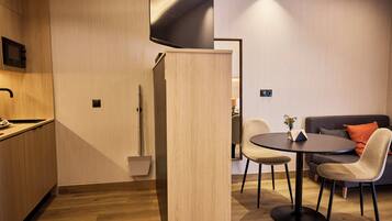 A modern kitchen with wooden cabinetry, a dining area with a round table and chairs, and a sofa in the background.
