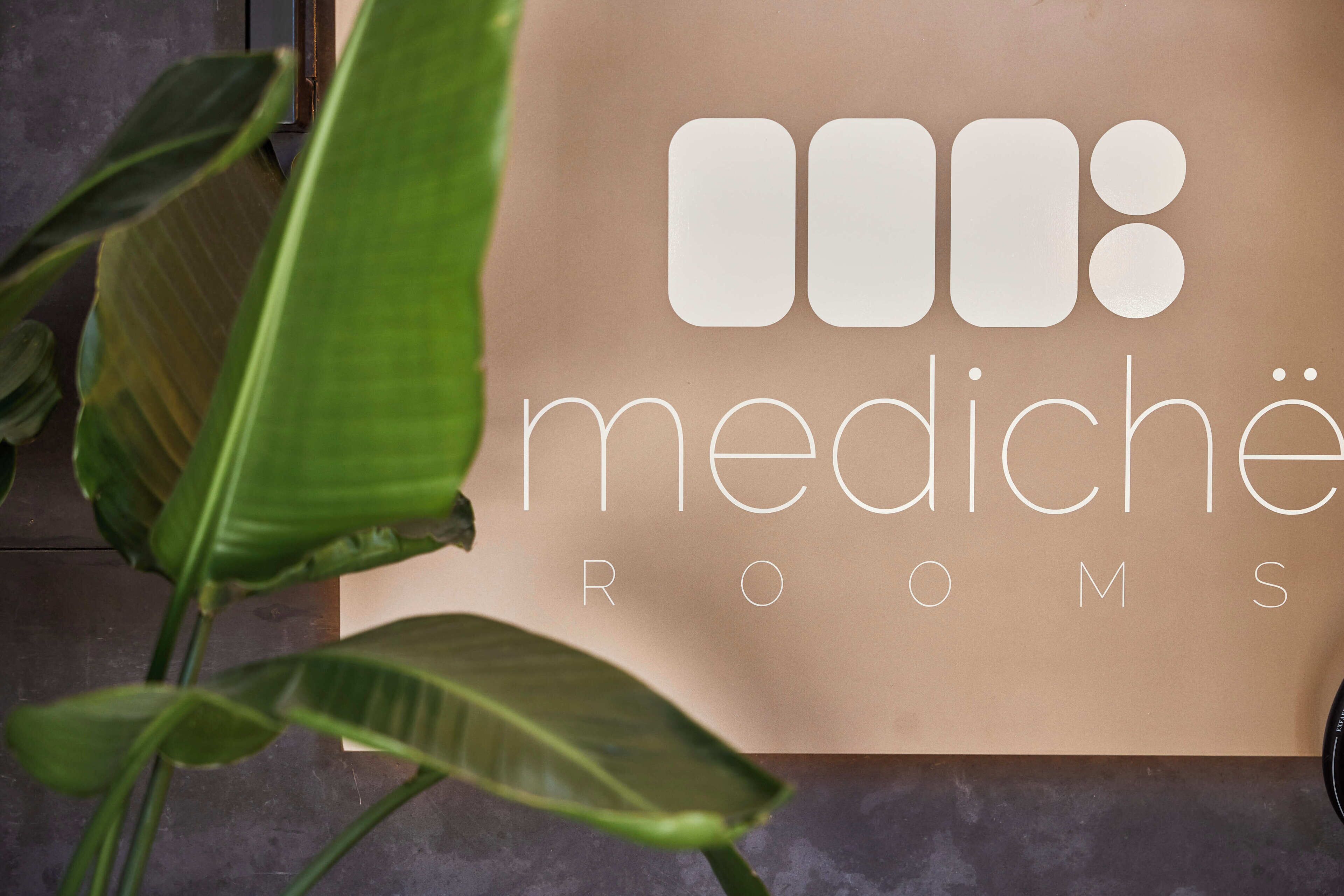 A sign with the text 'medische rooms' on a brown background, partially obscured by green plant leaves.