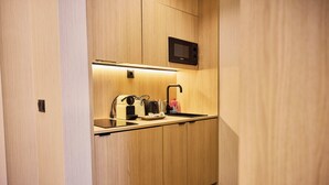 A compact kitchen with a microwave, kettle, and kettle stand.
