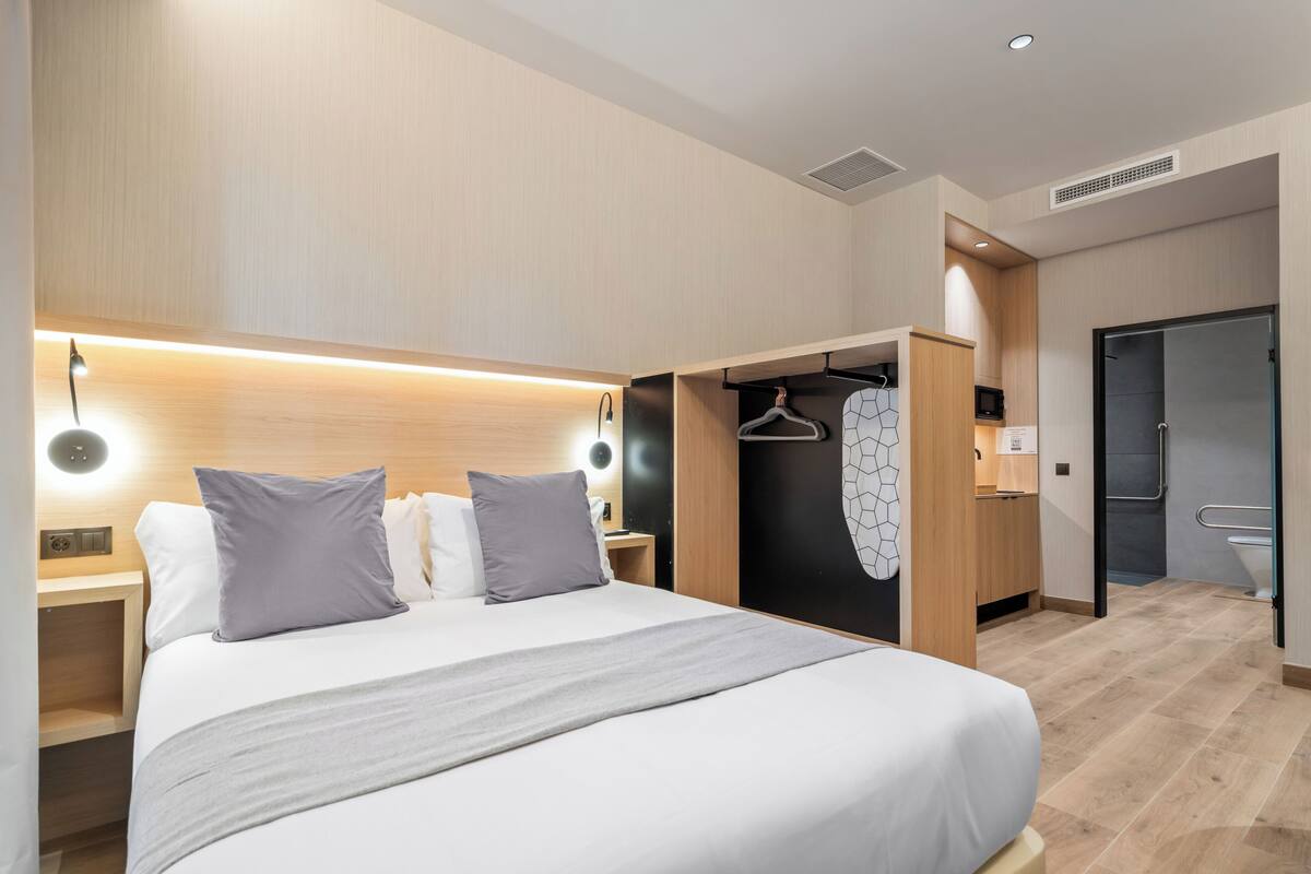 A modern hotel room with a large bed, bedside tables, a wardrobe, and a bathroom.