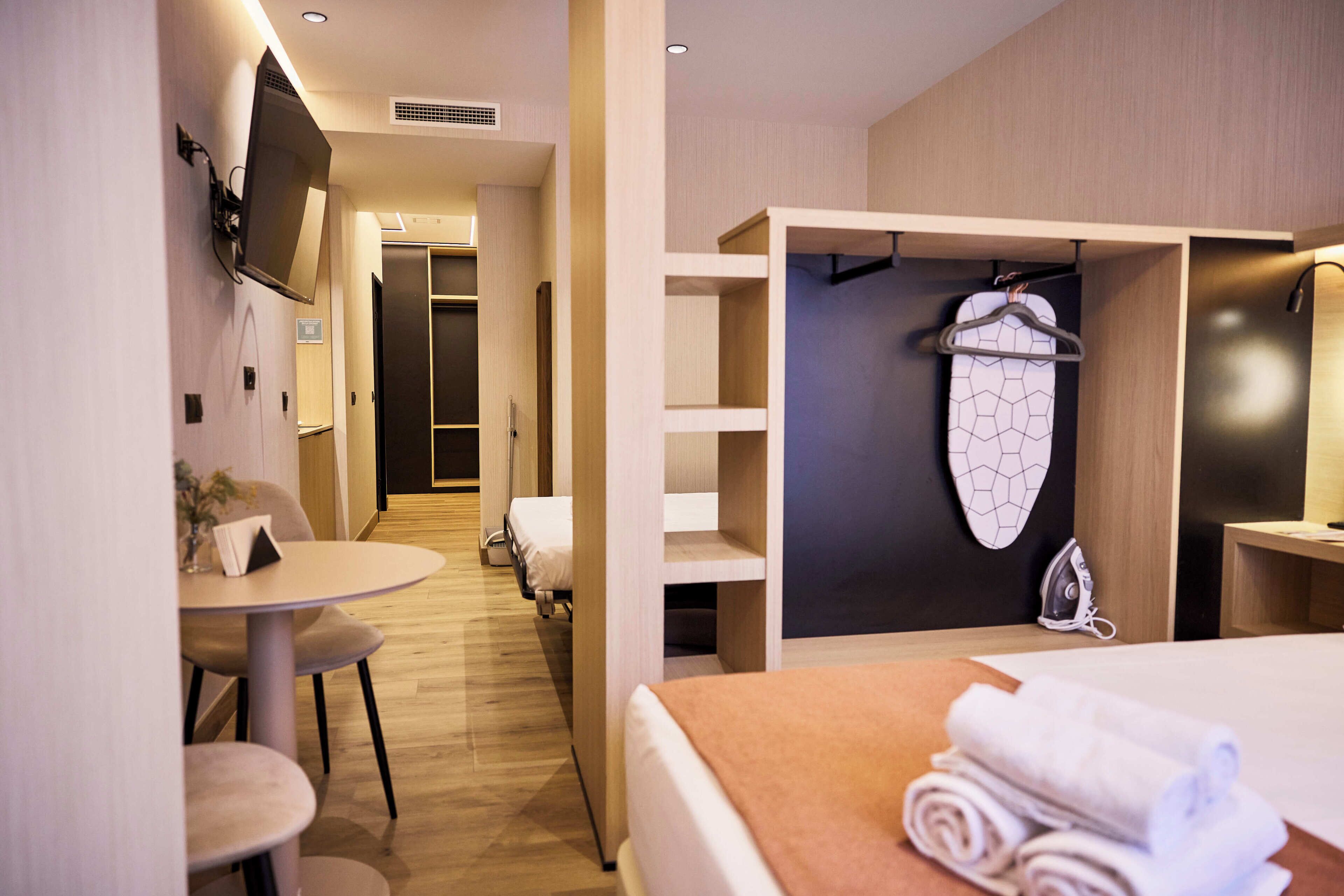 Habitación de hotel con cama, una mesa, sillas, perchero y zona de ducha.