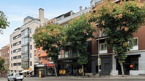 A multi-story building with a modern facade, a visible storefront with a sign, and a tree in front.