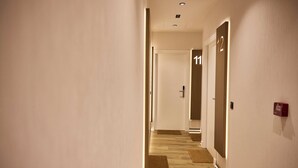 A hotel hallway with doors numbered 11 and 12, wooden flooring, and a fire alarm on the wall.