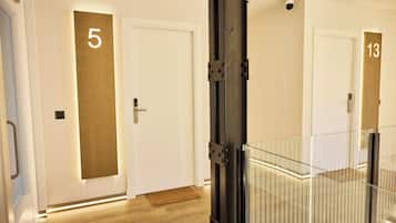 A hotel corridor with doors numbered 5 and 13, a metal gate, and a wooden floor.