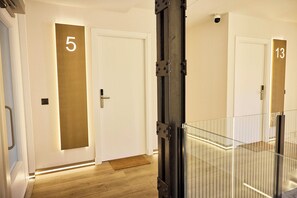 A hotel corridor with doors numbered 5 and 13, a metal gate, and a wooden floor. - Medichë Rooms General Ricardos (Madrid)