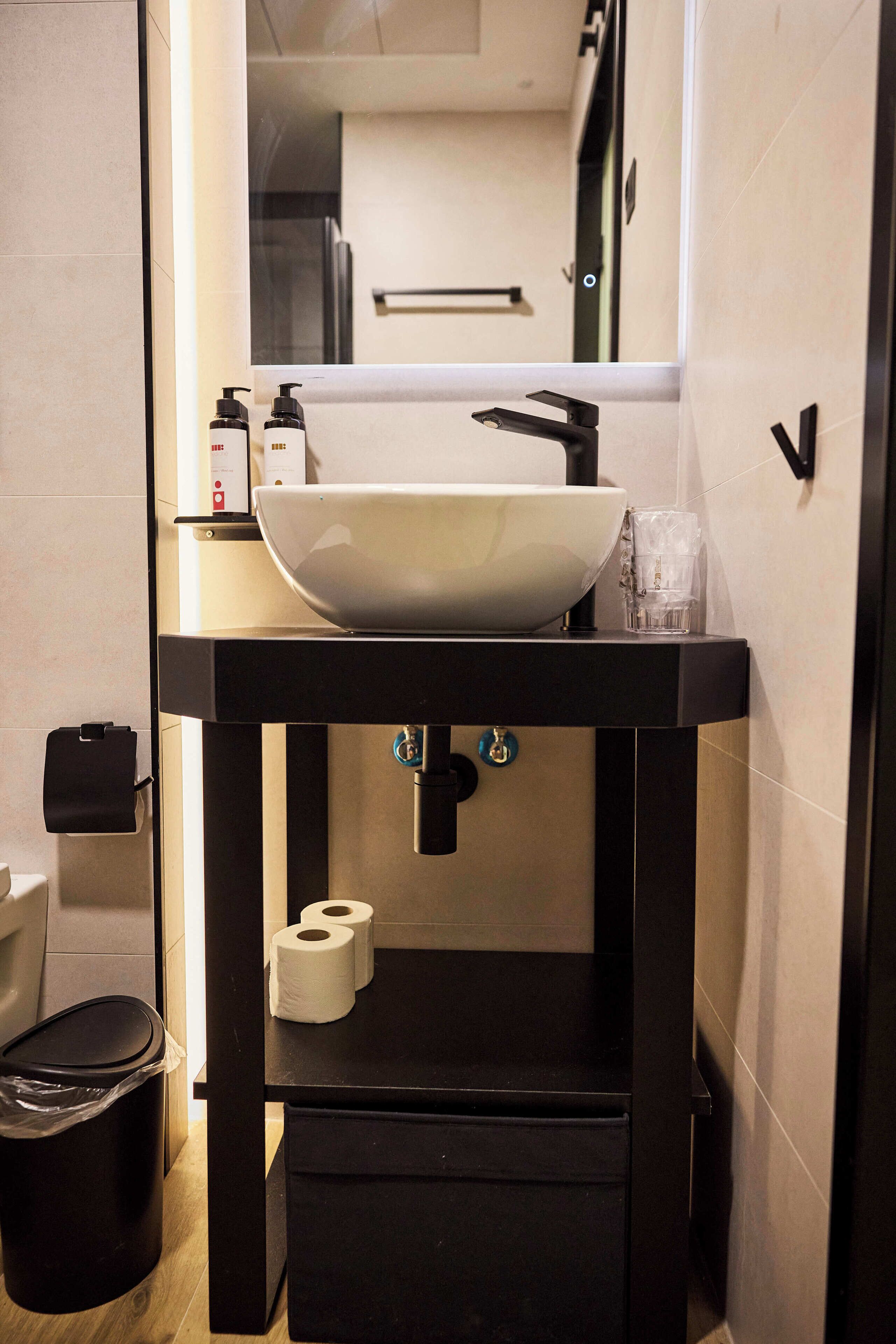 A bathroom with a white sink, black countertop, and a mirror above it. There are two rolls of toilet paper on the counter.