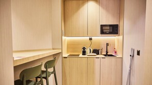 A compact kitchenette with a microwave, kettle, toaster, and sink. There are two green chairs and a small countertop.