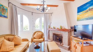 Una sala de estar acogedora con un sofá, una silla, una mesa de centro de vidrio, una chimenea, un televisor y un cuadro en la pared.