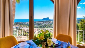 Un comedor con una mesa lista para dos personas, vista al mar y una montaña distante.