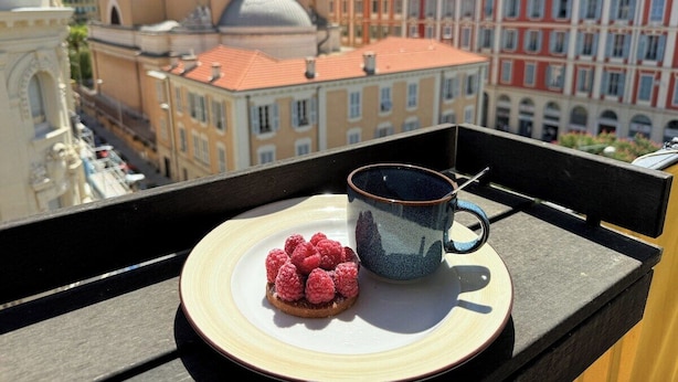 Un balcone con un piatto di lamponi e una tazza, affacciato su un panorama urbano con edifici storici.