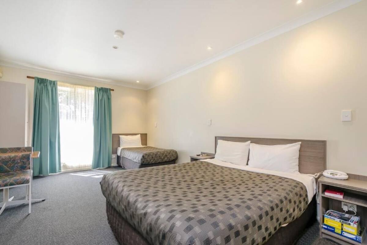 A hotel room with a large bed, a smaller bed, a chair, a desk with a phone, and a bookshelf.