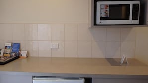 Une cuisine équipée d’un four à micro-ondes, d’un réfrigérateur et d’un plan de travail recouvert de carreaux.