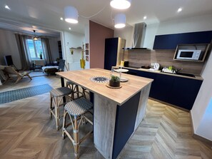 Eine moderne Küche mit einer zentralen Kochinsel, Barhocker, einer Mikrowelle und einem Essbereich mit einer Couch und Stühlen.