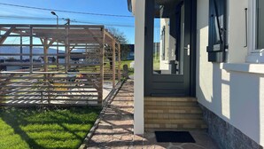 Una casa moderna con una porta d'ingresso scura, un pergolato in legno e un vialetto lastricato che conduce all'ingresso.
