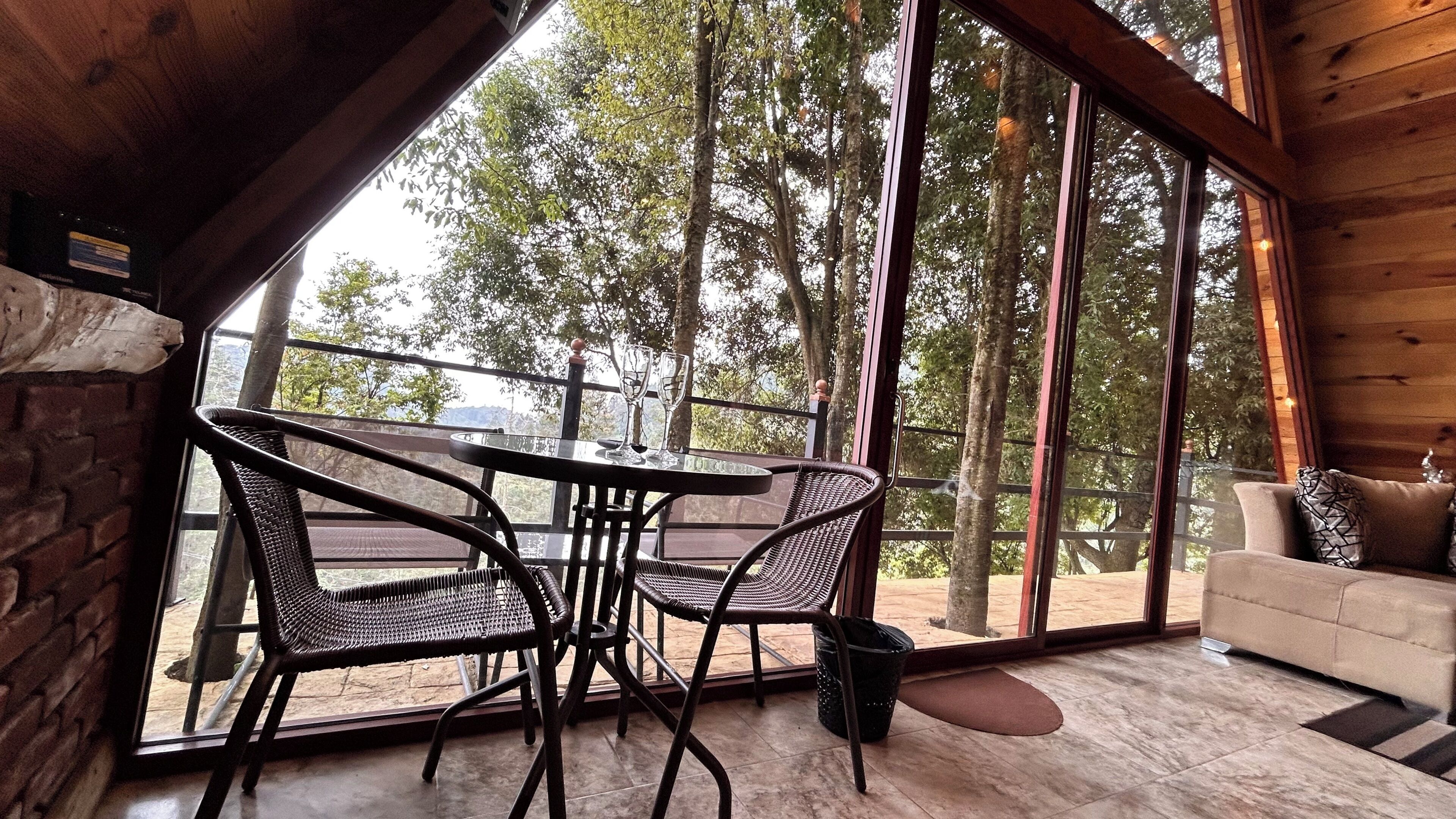 A wooden interior with a glass door leading to a balcony, wicker chairs, a round table, and a sofa.