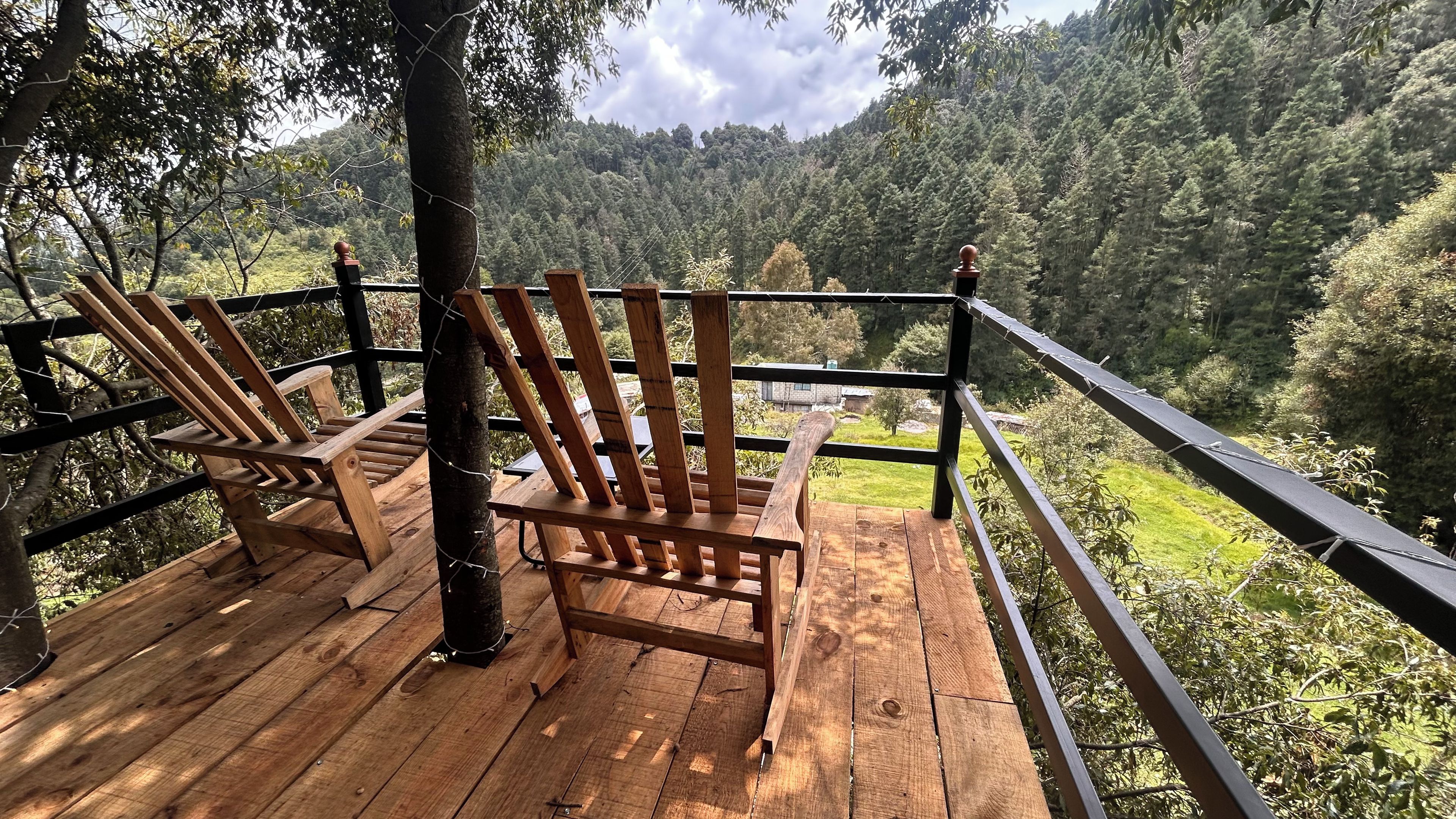 A wooden deck with two wooden chairs and a railing overlooking a forested hillside.