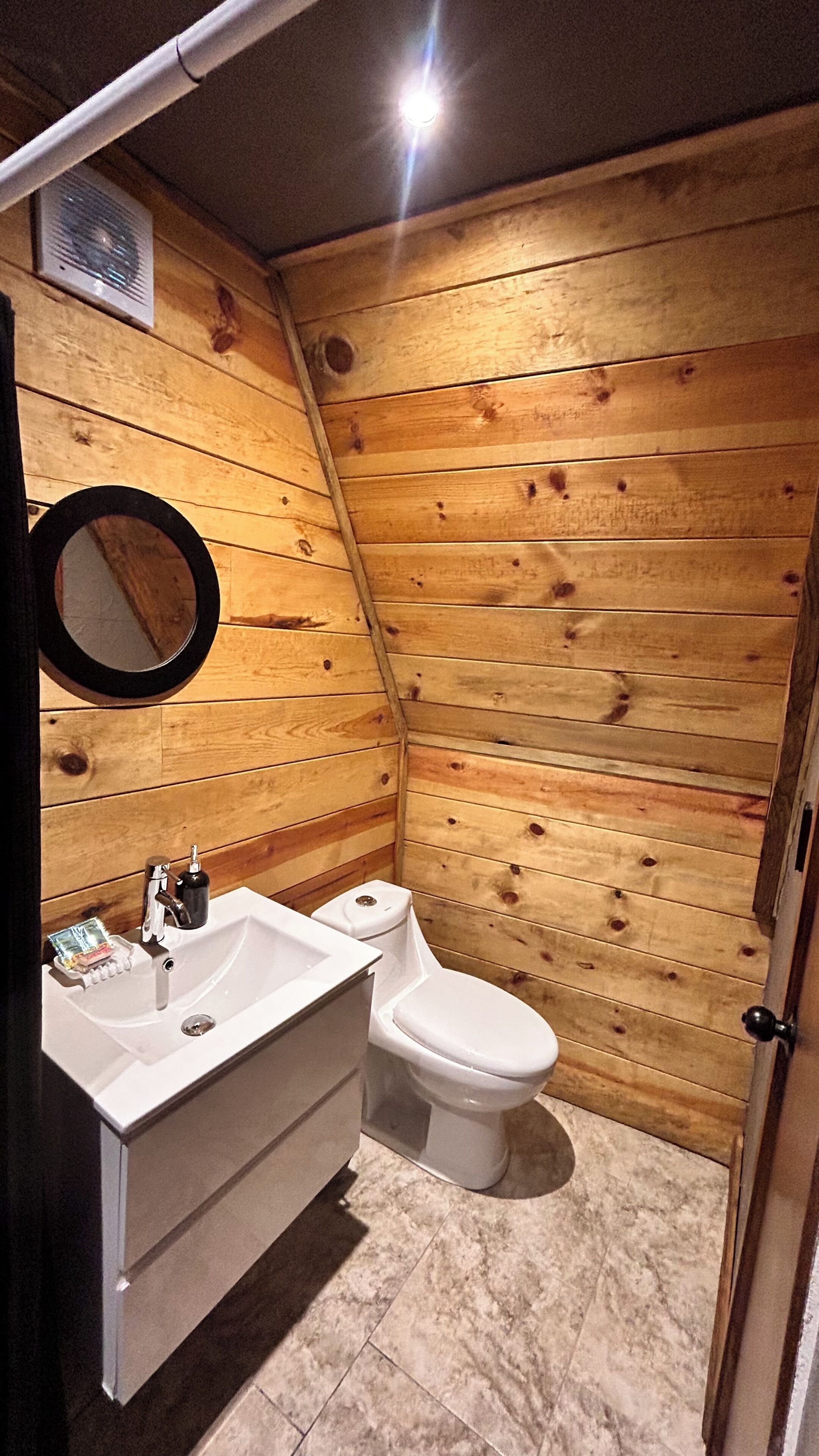 A wooden-paneled bathroom with a sink, mirror, and toilet.