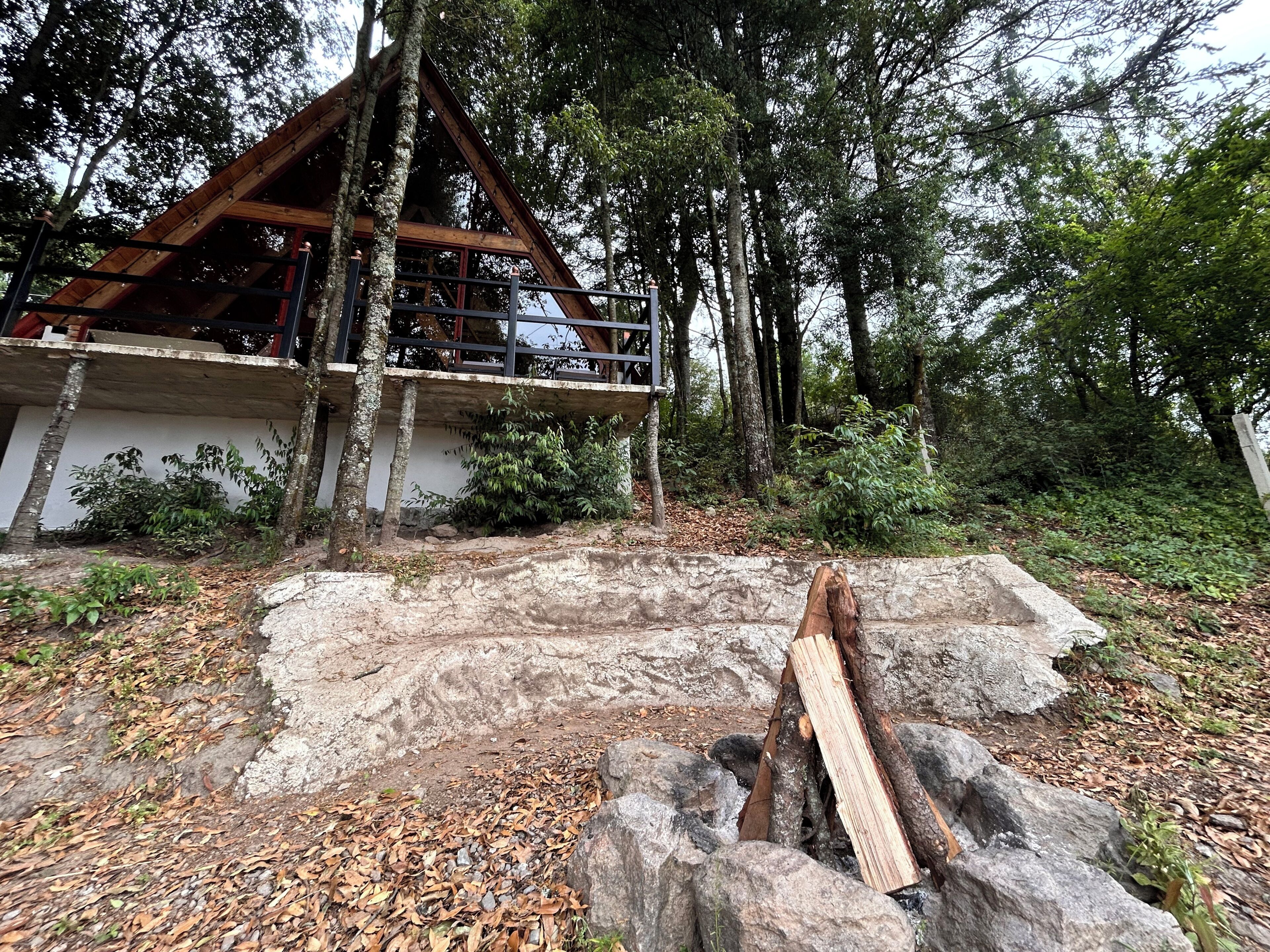 A cabin with a wooden deck, surrounded by trees and a stone wall.