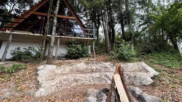 A cabin with a wooden deck, surrounded by trees and a stone wall.