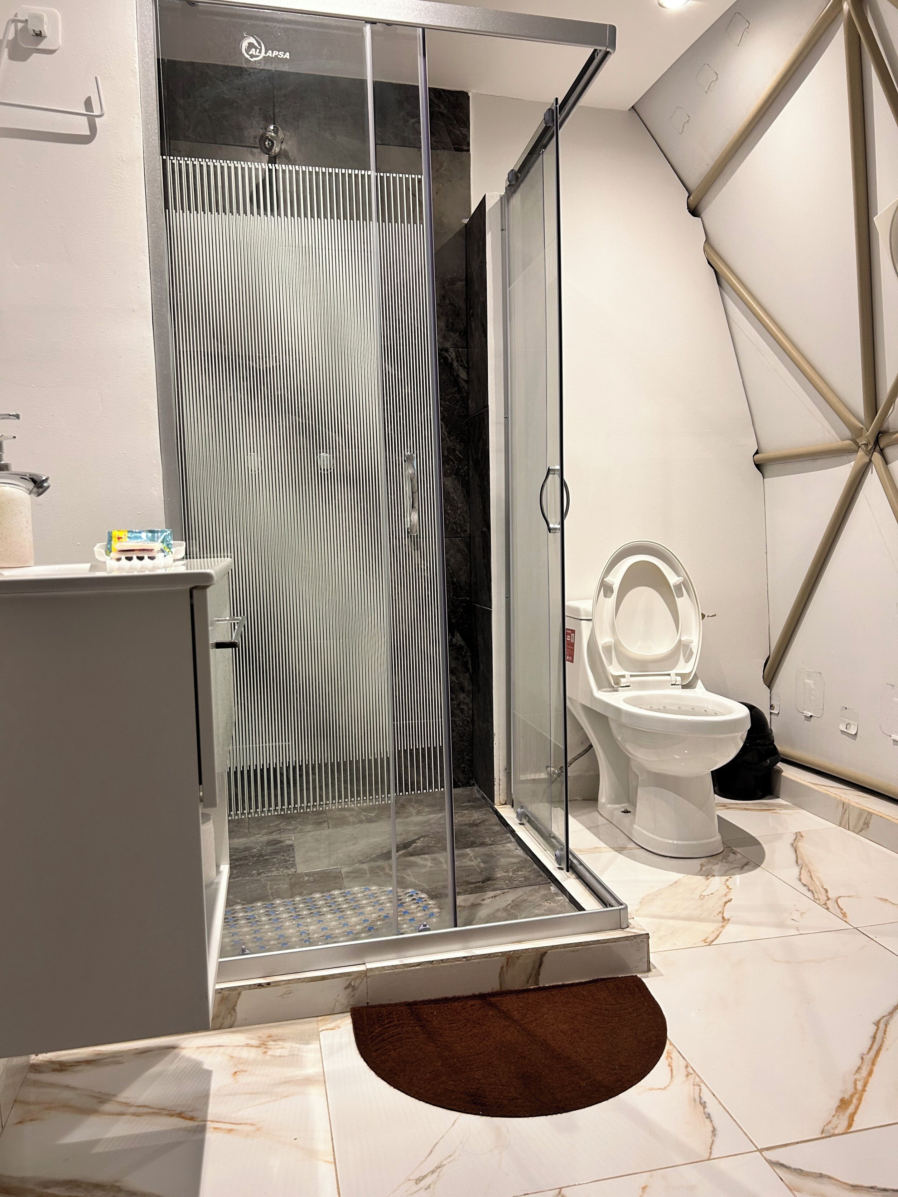 A modern bathroom with a glass-enclosed shower, a toilet, and a marble-tiled floor.