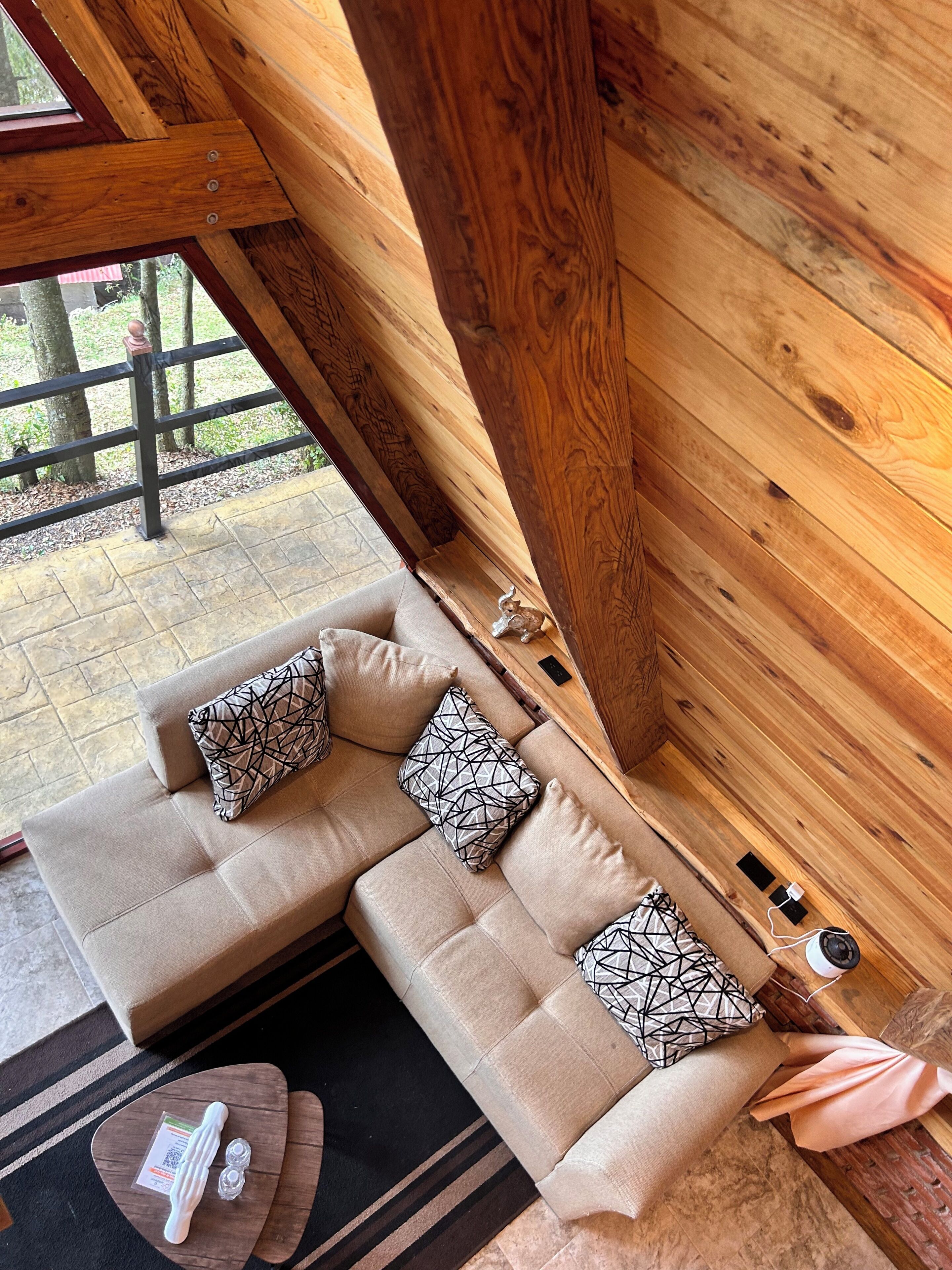 A wooden interior with a sofa, pillows, a small table, and a window view.