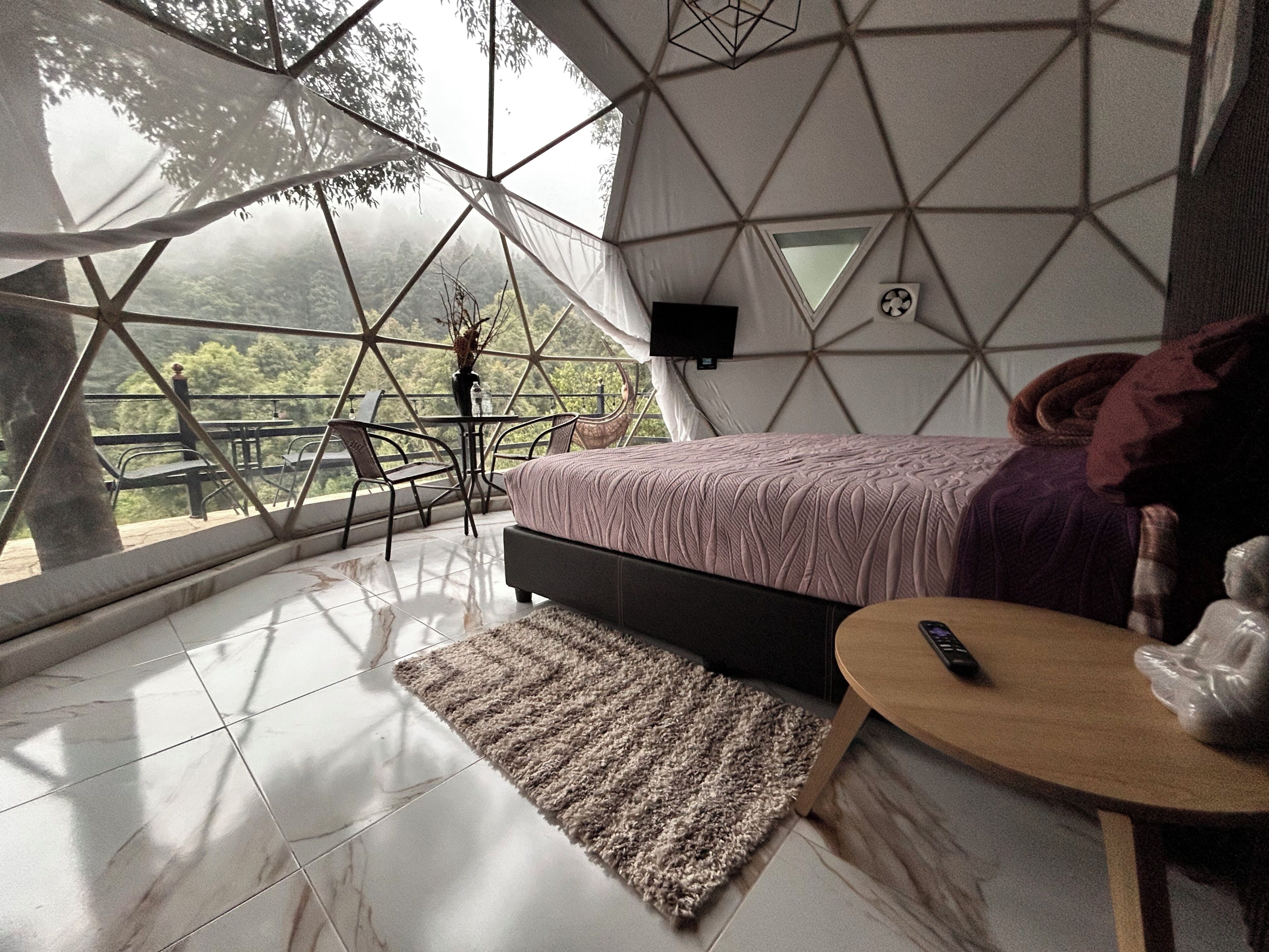 Una habitación con una cama, una mesita, una silla, una alfombra y un televisor.