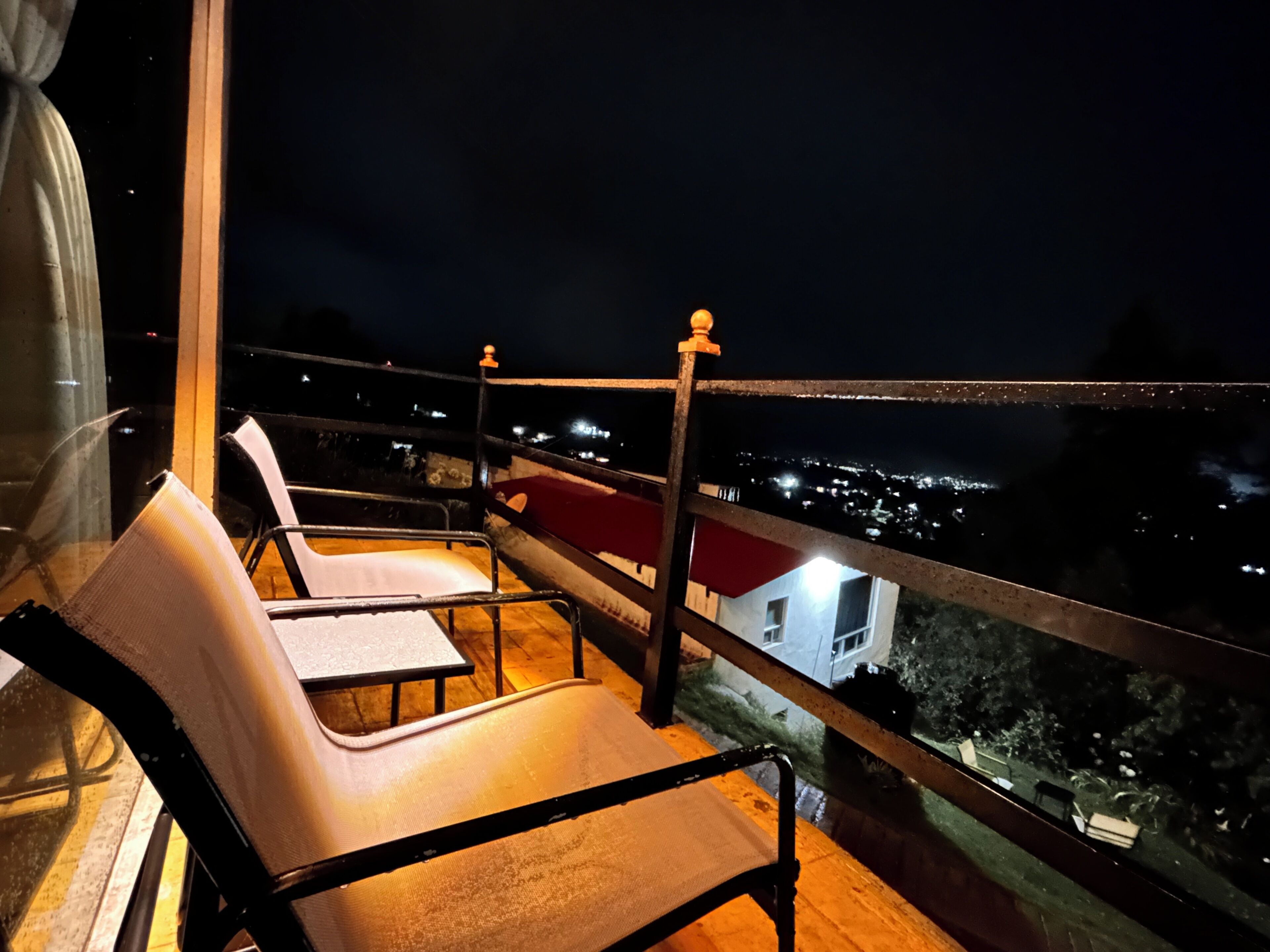 A balcony with chairs and a railing overlooking a cityscape at night.
