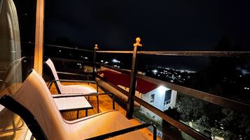 A balcony with chairs and a railing overlooking a cityscape at night.