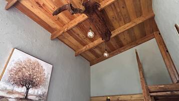 A rustic kitchen with wooden beams, a hanging light fixture, and a painting of a tree.