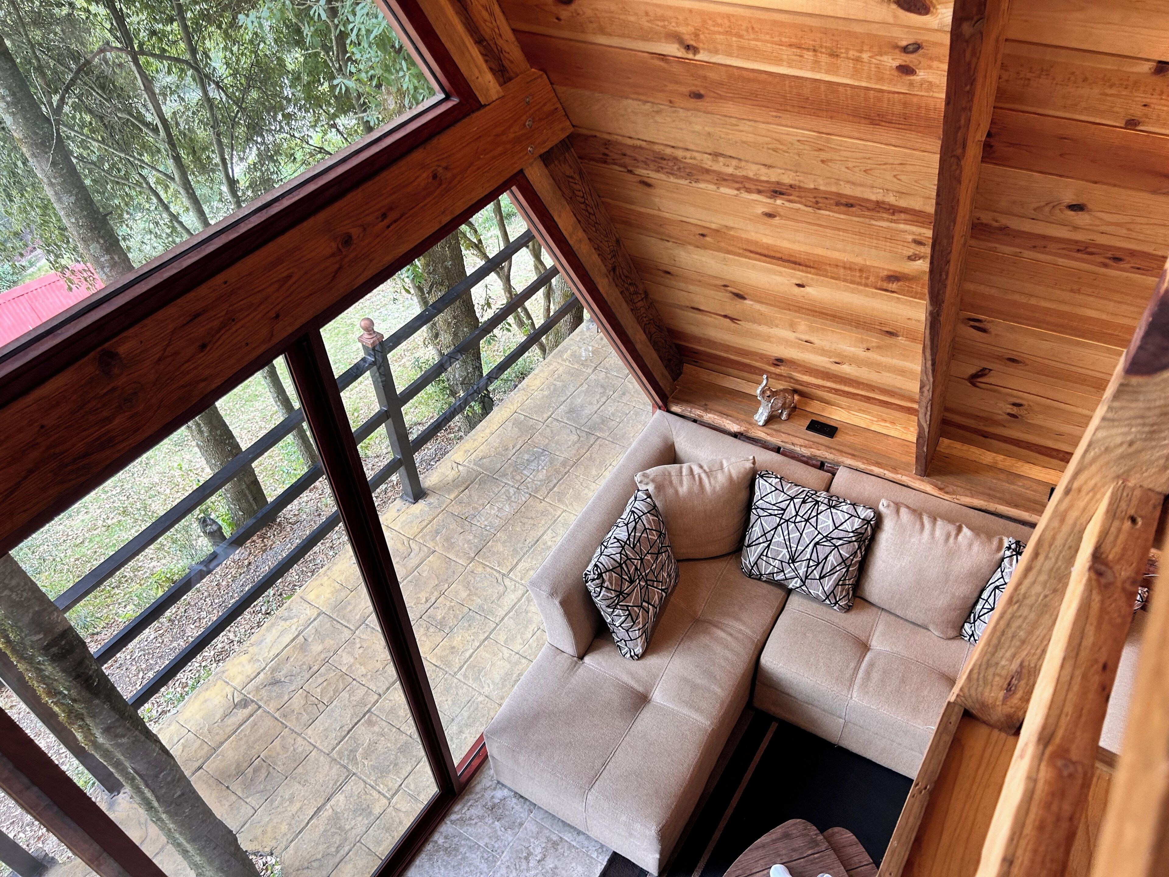 L’intérieur d’un chalet en bois, avec un canapé, des coussins et une vue sur l’extérieur.