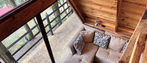 L’intérieur d’un chalet en bois, avec un canapé, des coussins et une vue sur l’extérieur.