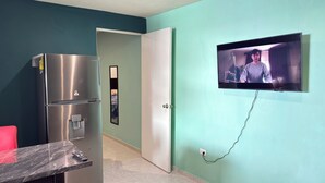 A modern kitchen with a stainless steel refrigerator, a marble countertop, and a wall-mounted TV.