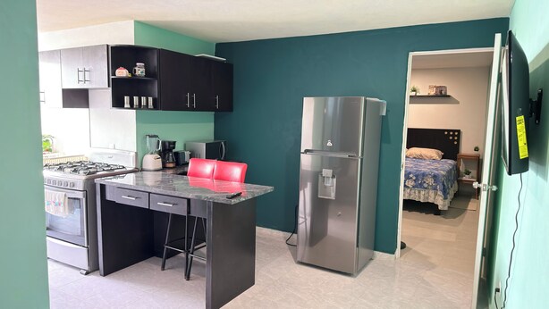 A compact kitchen with a gas stove, refrigerator, and a small dining area with a red chair.