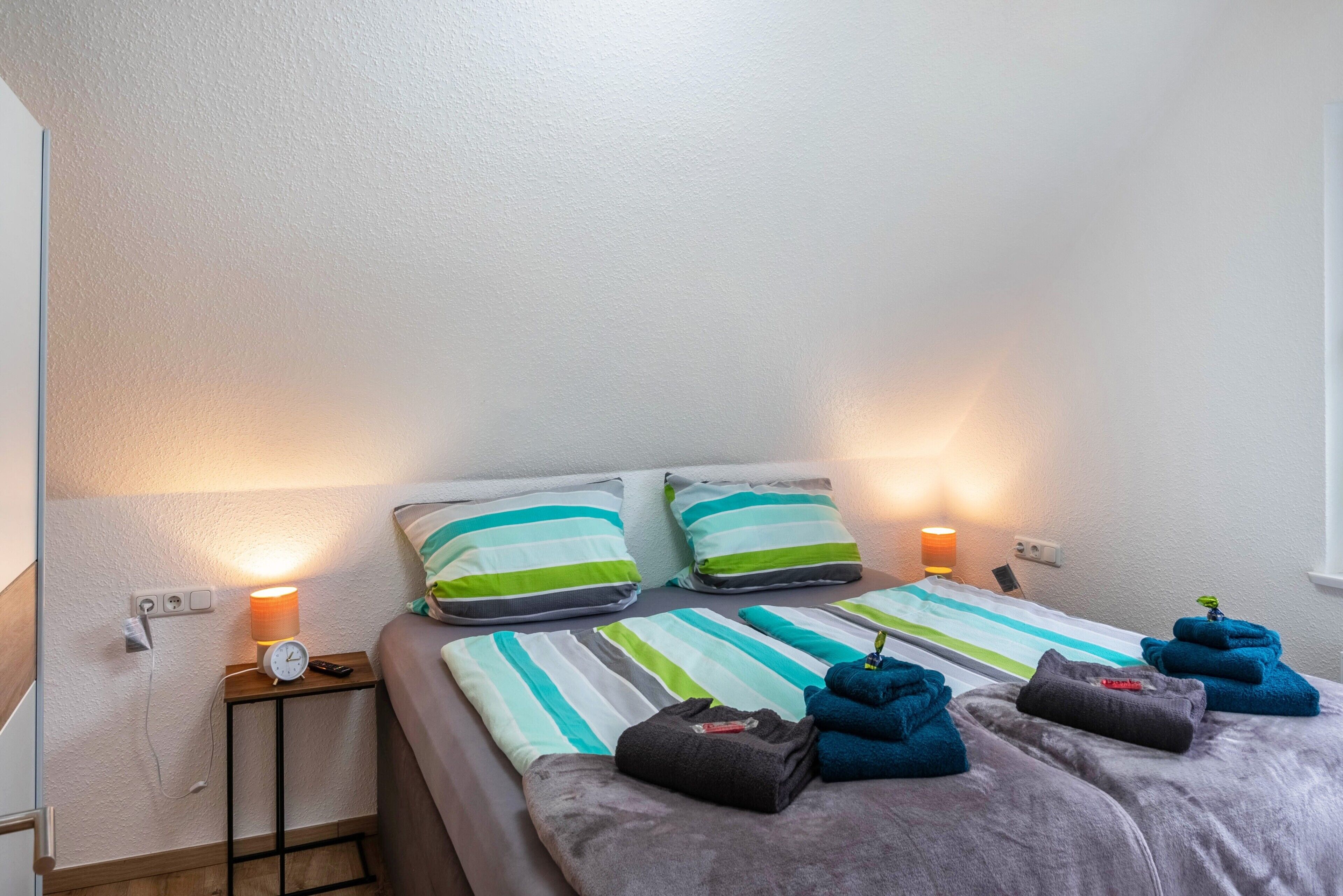 Une chambre d’hôtel avec deux lits, une literie à rayures, des oreillers, une table de chevet avec une lampe et des serviettes.