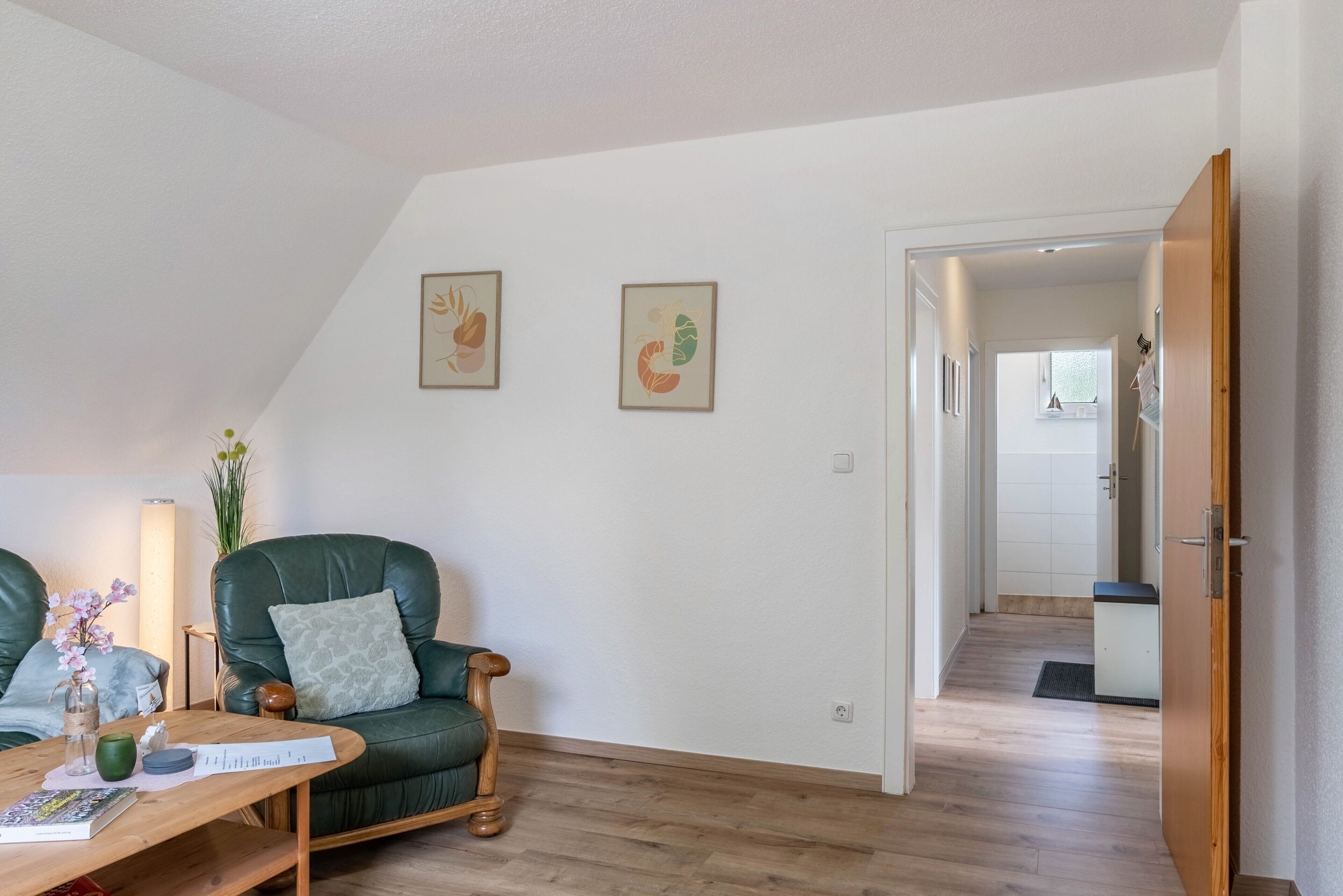 Een kamer met een groene leren fauteuil, een houten tafel met een vaas en een boek, en twee prestaties aan de muur.