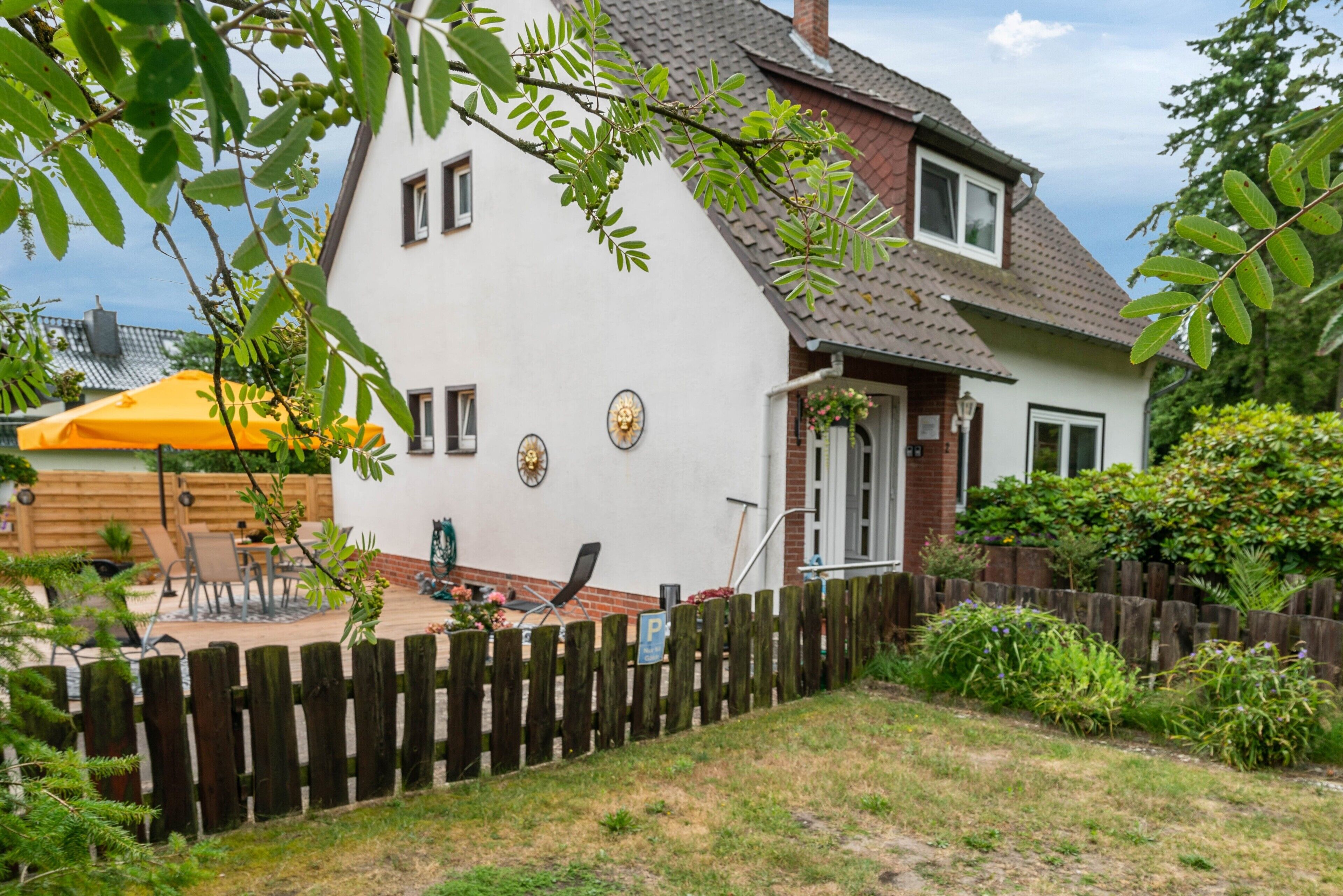 A two-story house with a white exterior, a wooden deck, and a fenced backyard.