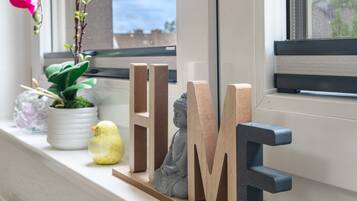Eine Fensterbank mit Dekorationsobjekten, darunter Holzbuchstaben, die ‚HOME‘ buchstabieren, und eine kleine Buddha-Statue.