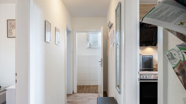 A narrow hallway leading to a kitchen with a refrigerator, oven, and microwave.