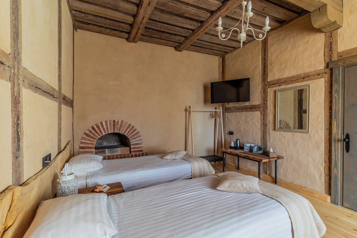 Una habitación rústica con dos camas, una chimenea de ladrillo, un televisor y un techo de madera.